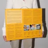 A person holds a yellow box with product information and images. Produktbild-Vorschau