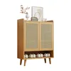 A wooden shoe cabinet with rattan doors and shelves, decorated with a vase and a framed picture on top. Produktbild-Vorschau
