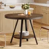 A round dining table with a shelf underneath, set in a kitchen or dining area with cabinets and chairs. Produktbild-Vorschau