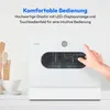 A white countertop dishwasher with a hand pressing a button on its control panel. Kitchen utensils and a cup are visible on the left. Produktbild-Vorschau