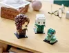 Three LEGO BrickHeadz figures are displayed on a wooden table, with a wooden box and other items in the background. Produktbild-Vorschau