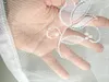 A hand is visible through a white lace curtain with floral embroidery. Produktbild-Vorschau