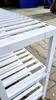 A close-up view of a white wooden shoe rack with multiple slatted shelves, placed outdoors on a paved surface. Podgląd zdjęcia produktu