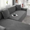 A grey sectional sofa with a leaf pattern, covered in a stretchable fabric. A coffee cup and saucer sit on a newspaper on the sofa. Produktbild-Vorschau