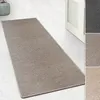 A taupe runner rug with a sisal-like texture is laid out on a light-colored floor, with a partially open white door in the background. There are also smaller inset images showing different color variations of the rug. Produktbild-Vorschau