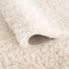 A close-up view of a cream-colored shaggy rug, with a corner folded back to reveal the underside. Produktbild-Vorschau
