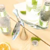 A metallic bottle opener shaped like a bird is placed on a wooden table next to bottles of drink, a glass, and citrus fruits. Podgląd zdjęcia produktu