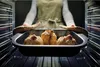 A person is placing a baking dish with food into an oven. Produktbild-Vorschau