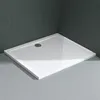 A white rectangular shower tray with a textured surface and a drain is shown in a bathroom setting with dark gray tiled walls and light gray tiled floor. Produktbild-Vorschau