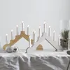 Two candle arches are displayed on a white tablecloth, with Christmas ornaments and a glass vase containing a small pine tree in the background. Podgląd zdjęcia produktu