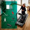 A woman is using a treadmill in a home environment, with various accessories and instructions laid out nearby. Produktbild-Vorschau