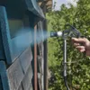 A hand is holding a Wagner electric paint sprayer and spraying a wooden structure outdoors. Náhled obrázku produktu