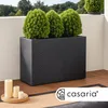 A black rattan planter with three green plants sits on a wooden deck. Candles are on a wooden tray in the foreground. Voir les images du produit