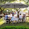 A group of people are gathered around a table outdoors under a large umbrella, possibly at a wedding reception or party. Náhled obrázku produktu