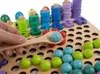 A hand is holding a wooden spoon with a light blue bead on it, over a wooden board with many holes. There are colorful beads and wooden number pieces on the board. Produktbild-Vorschau