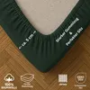 A close-up of a dark green fitted sheet corner, showing its elastic edge and texture, with informational text and icons. Produktbild-Vorschau
