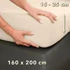 Hands are shown stretching a cream-colored fitted sheet over a mattress. Produktbild-Vorschau