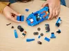 A child's hands are assembling a blue LEGO car on a wooden table. Podgląd zdjęcia produktu