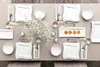 A table setting with white plates, cutlery, glasses, and a bouquet of white flowers. Produktbild-Vorschau