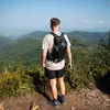A man stands on a mountain overlooking a valley, wearing a backpack. Náhľad obrázku produktu