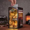 A hand is inserting a piece of paper into a miniature 3D book nook model of a train interior, with other vintage items in the background. Voir les images du produit