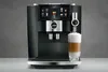A JURA coffee machine is shown on a gray background, with a latte being dispensed into a glass. Produktbild-Vorschau