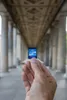 A hand holds a small SD card in front of a colonnade. Produktbild-Vorschau