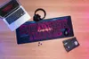 A collection of gaming and retro-themed items arranged on a wooden surface, including a laptop, headphones, a mousepad with 'Stranger Things' branding, a mouse, and a VHS tape. Produktbild-Vorschau