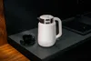 A white electric kettle and a black teacup are placed on a dark countertop in a kitchen setting. Voir les images du produit