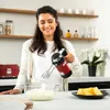 A woman is using a red hand mixer in a kitchen. Produktbild-Vorschau