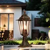 A classic outdoor lamp is lit in a garden at dusk, with a house and patio furniture in the background. Produktbild-Vorschau