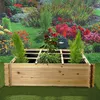 A wooden raised garden bed filled with plants, set against a backdrop of a colorful garden. Produktbild-Vorschau