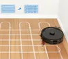 A black robot vacuum cleaner is shown on a wooden floor, cleaning up debris. The image also includes diagrams illustrating cleaning patterns. Produktbild-Vorschau