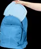 A hand is placing a light blue board game into a blue backpack. Produktbild-Vorschau