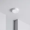A white, round LED ceiling light is mounted on a white ceiling, with two white walls meeting at a corner in the foreground. Produktbild-Vorschau