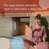 A woman sits on the floor holding a glass of water, with kitchen cabinets and a water filter in the background. A blue circular overlay contains text about water purity. Anteprima dell’immagine prodotto