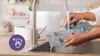 A person is washing a gray sterilizer part under a faucet in a kitchen sink. Produktbild-Vorschau