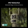 A camouflage trail camera mounted on a tree in a forest setting with rain falling. Produktbild-Vorschau