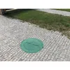A green manhole cover sits on a cobblestone path next to a patch of grass. Podgląd zdjęcia produktu