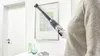 A person is using a cordless vacuum cleaner to clean the top edge of a framed picture on a wall. Voir les images du produit