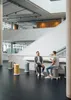 Two men are sitting and talking on stools in a modern office building atrium. Produktbild-Vorschau