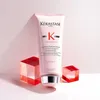 A pink Kérastase Genesis fondant renforçateur conditioner tube is displayed upright, centered in the frame. It is flanked by two transparent, faceted red acrylic cubes, one on each side, positioned slightly forward and to the sides of the tube. The backgro Náhled obrázku produktu
