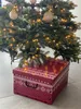 A red decorative box with white snowflake patterns sits under a decorated Christmas tree. Produktbild-Vorschau