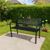 A black metal garden bench sits on a paved patio in a garden setting. Produktbild-Vorschau