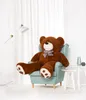 A large brown teddy bear sits in a light blue armchair in a brightly lit room with white curtains. Anteprima dell’immagine prodotto