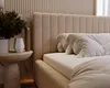 A close-up view of a beige bouclé upholstered bed with pillows and a bedside table with a plant and vase. Produktbild-Vorschau