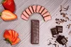 A top-down view of strawberries and chocolate-covered wafers arranged on a striped wooden surface. Produktbild-Vorschau