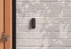 A black keypad is mounted on a light gray brick wall next to a wooden door. Voir les images du produit