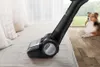 A vacuum cleaner head is shown cleaning a sofa, with a dog lying on the wooden floor in the background. Náhled obrázku produktu