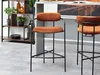 Two bar stools with copper-colored seats and black metal frames are shown in a modern interior setting. Náhľad obrázku produktu